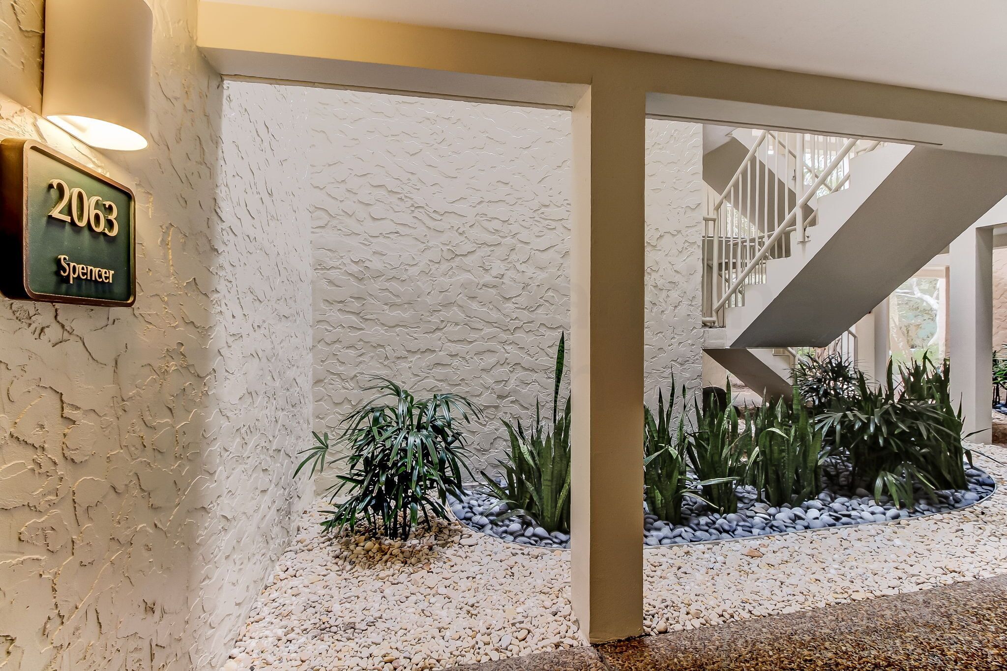 Une entrée moderne, avec un mur à texture, une enseigne indiquant « 2063 Spencer » et un escalier menant à un niveau supérieur.