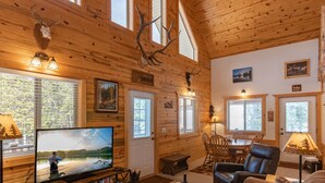 Ein Holzblockhaus-Innenraum mit Fernseher, Holzmöbeln und Hirschgeweihen an der Wand.