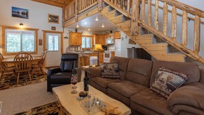 Ein gemütliches Wohnzimmer mit einer Holztreppe, einem Essbereich mit Tisch und Stühlen sowie einer Küche im Hintergrund.