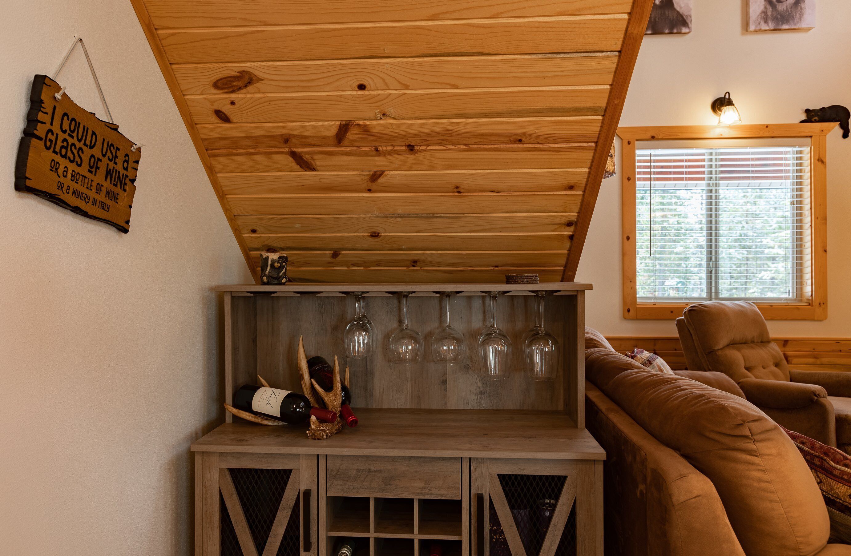 Un plafond en bois avec une enseigne, un meuble à vin avec des verres et un canapé marron.