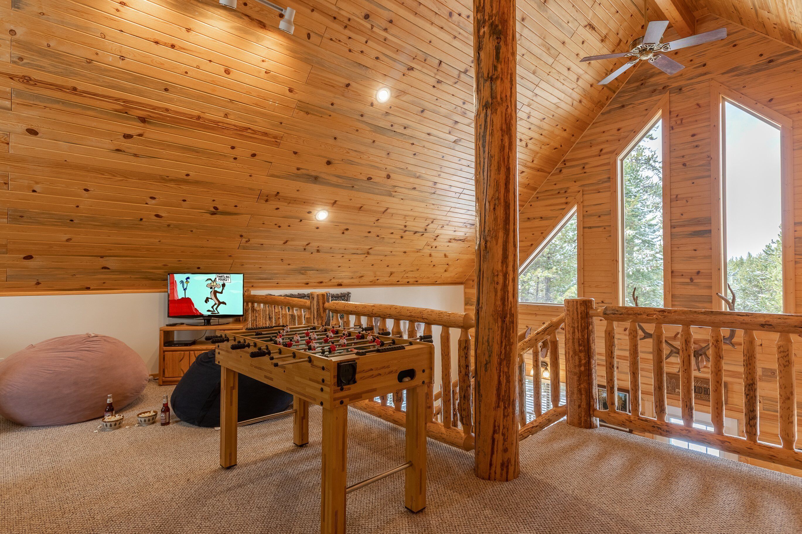 A cozy room with a wooden ceiling, a foosball table, a television, and a large window.
