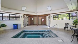 En inomhuspool med ett kaklat golv, en central trappa och en sittgrupp med bord och stolar.