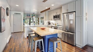 Ett modernt kök med rostfria vitvaror, en köksö i trä och barstolar.