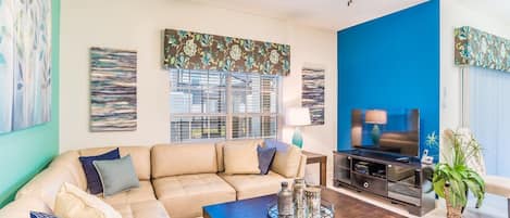 A living room with a beige sofa, a coffee table with salt and pepper shakers, a TV, and a blue accent wall.
