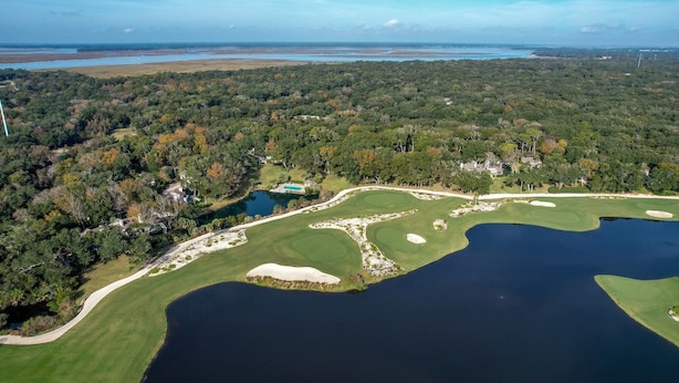 Vista aerea di un campo da golf con diverse bunker, uno stagno e zone boschive circostanti.