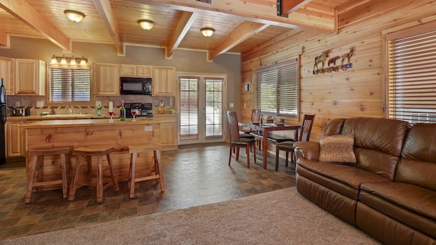 A spacious kitchen with wooden cabinets, a central island with stools, and a dining area with a leather couch. - Rimfire Refuge (Island Park)
