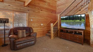 A wooden interior with a leather sofa, a television on a wooden stand, and a staircase. - Rimfire Refuge (Island Park)