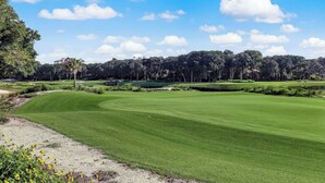 Ein Golfplatz mit blauem Himmel, Bäumen und einem Gebäude in der Ferne.