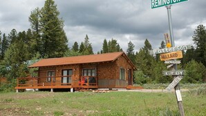 A rustic cabin with a wooden deck, surrounded by dense forest. - True Grit Adventure (Island Park)