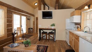 A compact kitchen with a TV, wooden cabinets, and a dining area with chairs and a table. - True Grit Adventure (Island Park)