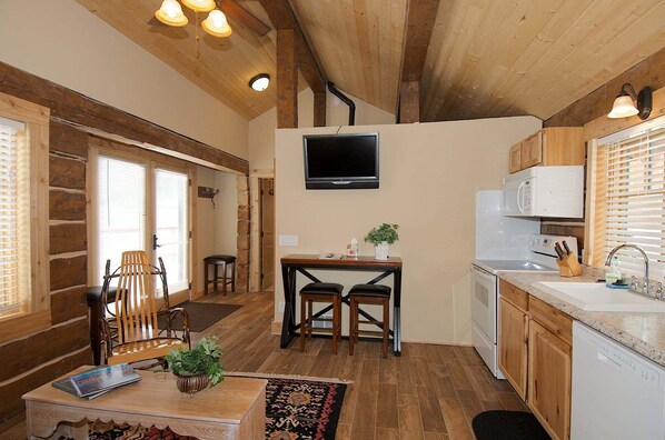 A compact kitchen with a TV, wooden cabinets, and a dining area with chairs and a table. - True Grit Adventure (Island Park)