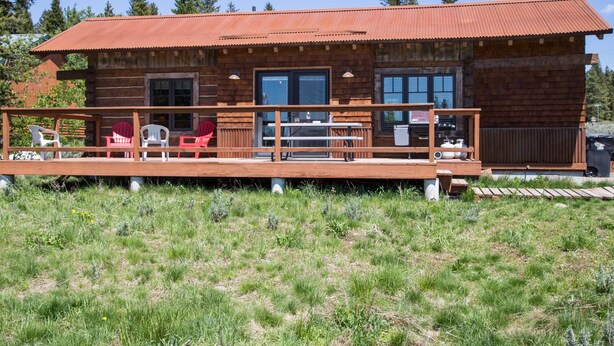 A rustic cabin with a wooden deck, a covered outdoor seating area, and a metal roof. - True Grit Adventure (Island Park)