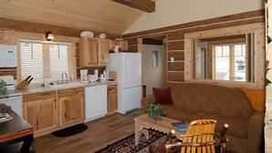 A cozy cabin-style interior with wooden beams, a kitchenette, a dining area, and a living room with a sofa and a chair. - True Grit Adventure (Island Park)