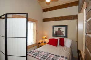 A bedroom with a bed, a nightstand, a lamp, a window with blinds, and a framed picture on the wall. - True Grit Adventure (Island Park)