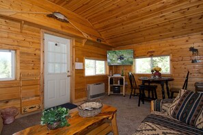 Interior de una cabaña de madera con comedor, televisor y un rincón de estar acogedor.