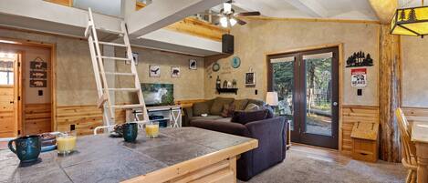A cozy cabin interior with a wooden loft, a dining area, and a living room.