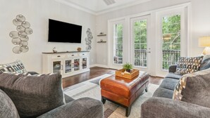 A spacious living room with a large flat-screen TV, a white cabinet with glass doors, and a large sliding glass door leading to a balcony. - 905 Summerwoods Cir (Fernandina Beach)