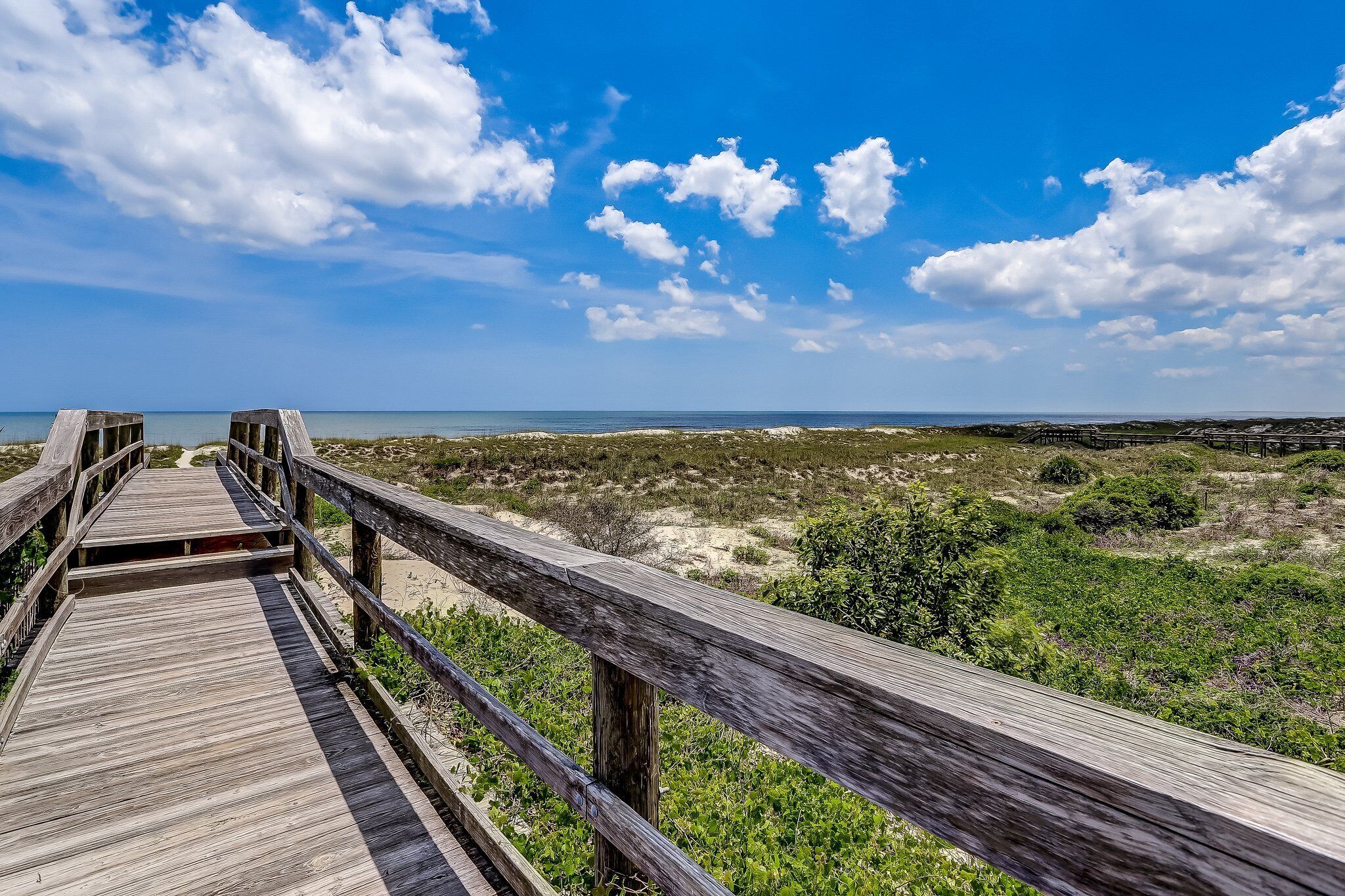 A wooden boardwalk leading to a beach with a clear sky and distant horizon.