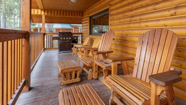 A wooden cabin with a porch, wooden chairs, a grill, and a window. - Remington Reload (Island Park)
