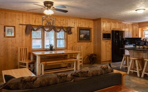 Un intérieur en bois comprenant une table à manger, des chaises, un canapé, un ventilateur de plafond et un coin cuisine.