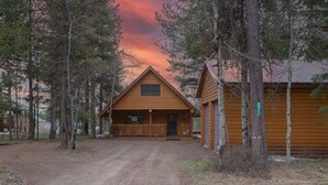 A wooden cabin with a porch, surrounded by trees, and a dirt road leading to it. - Remington Reload (Island Park)