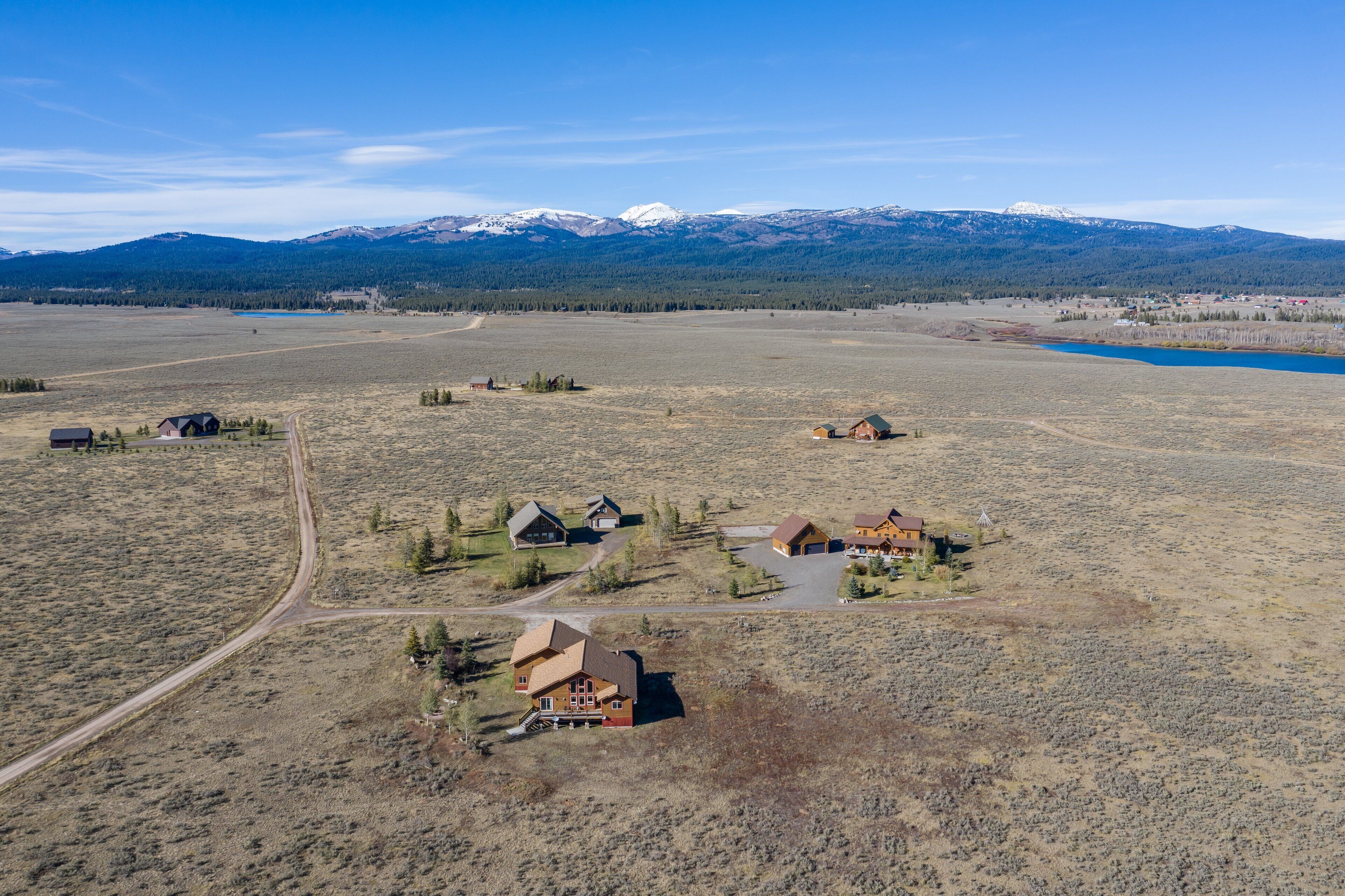 An aerial view of a rural property with multiple buildings, a dirt road, and a lake.