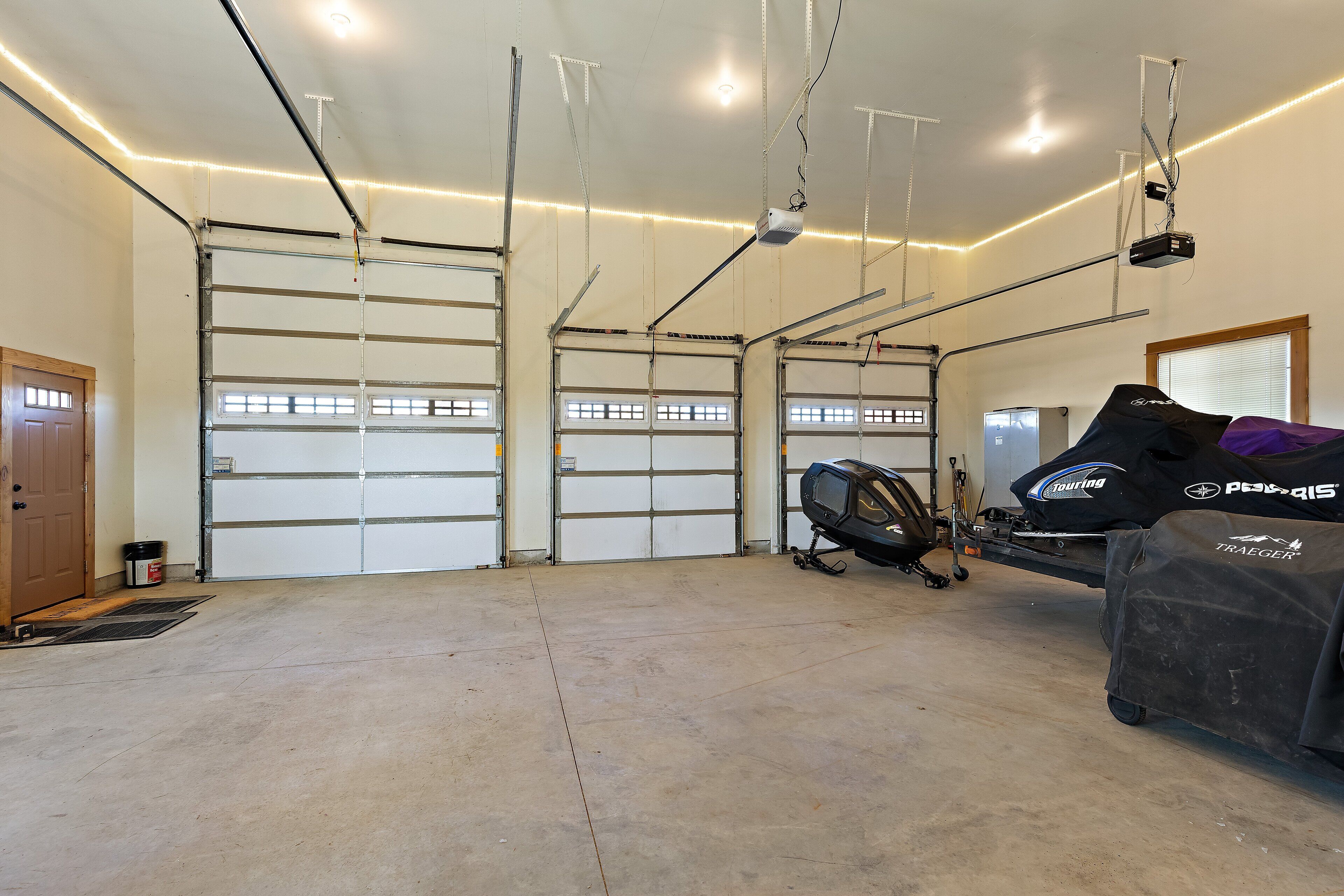 A garage with three large garage doors, a ceiling-mounted projector, and a covered vehicle with branding.