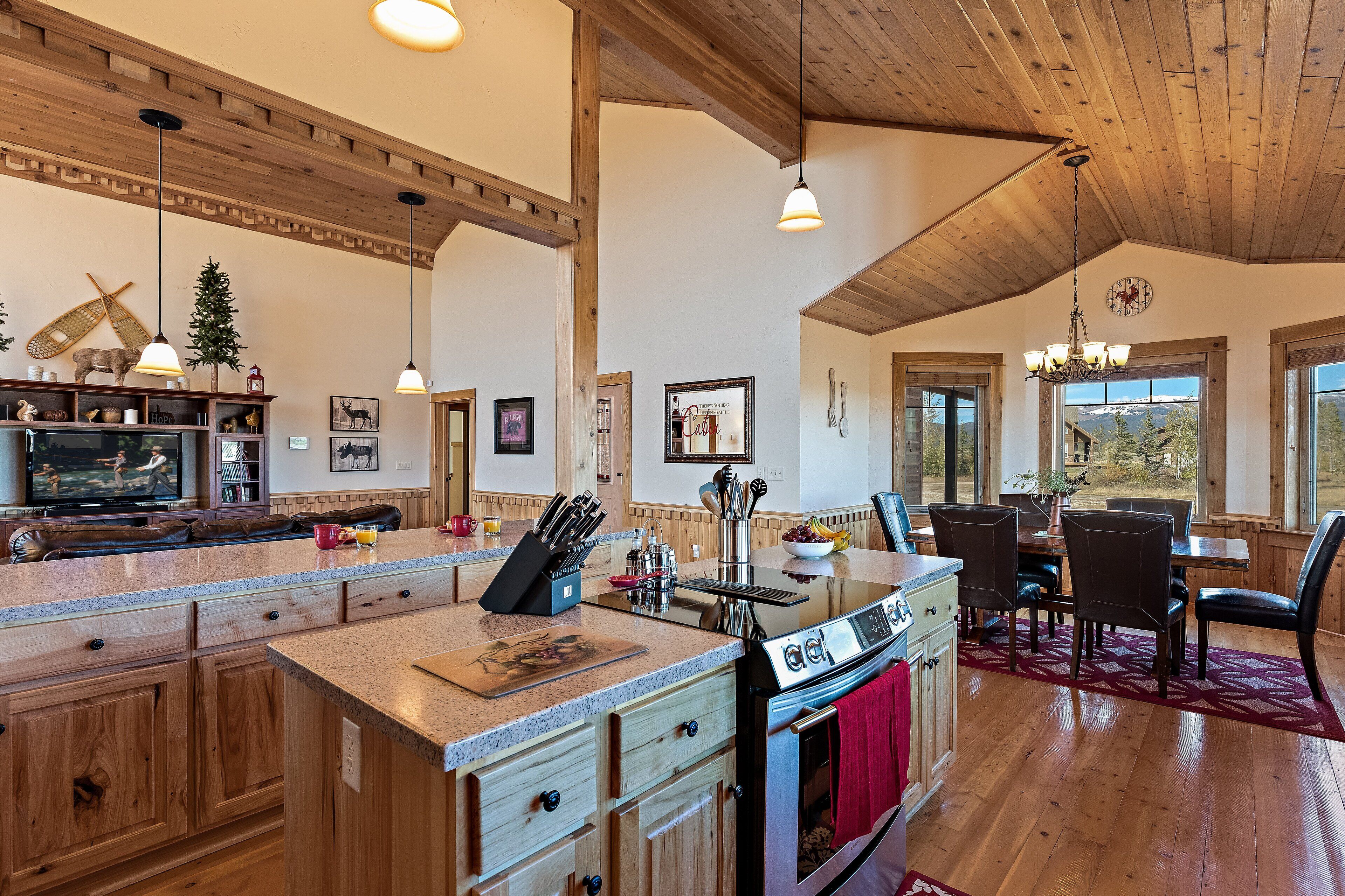A spacious kitchen with wooden cabinets, a large island, and a dining area with a red rug.