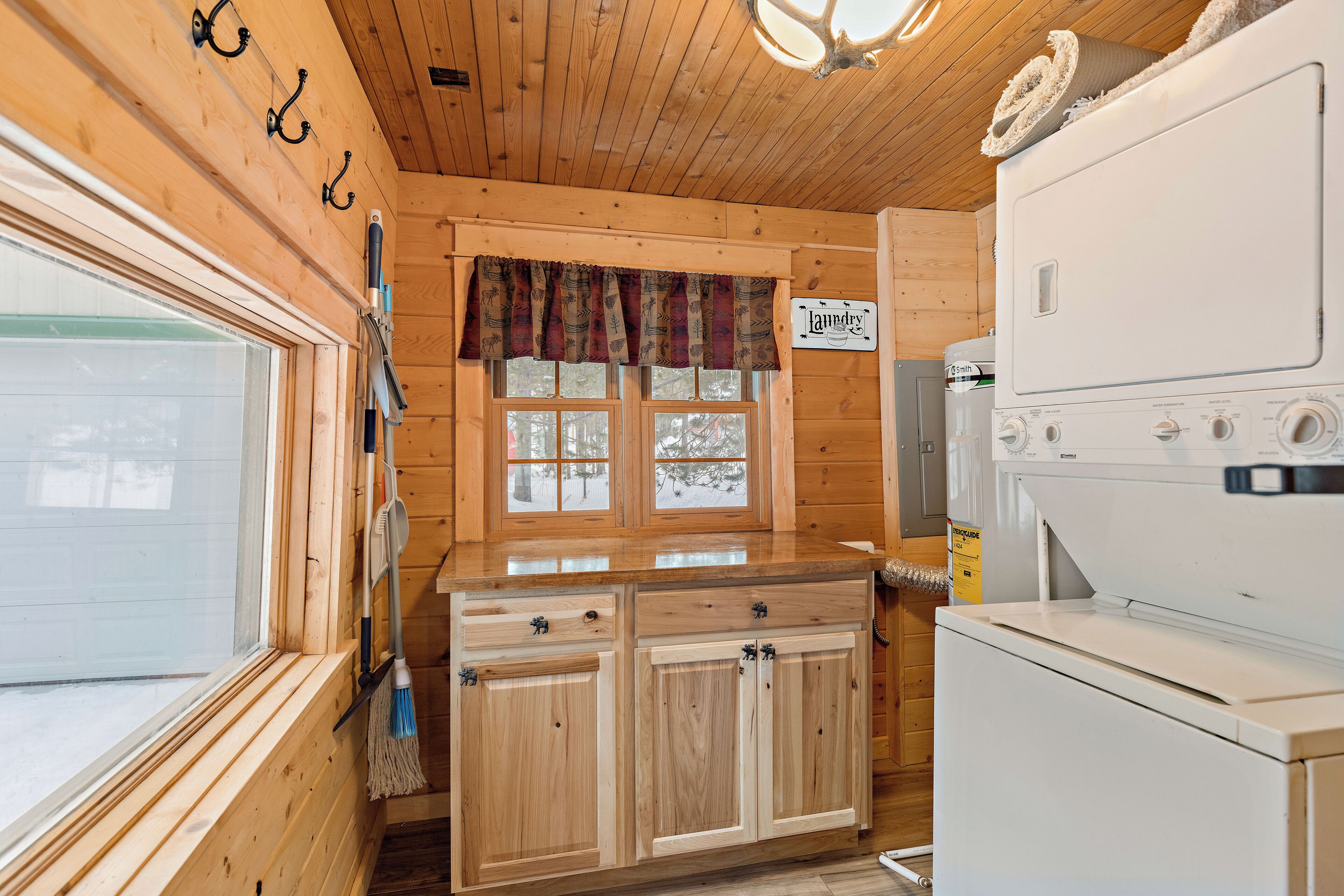 A wooden cabin interior with a kitchen area, including a wooden cabinet, a window with a view, and a washing machine.