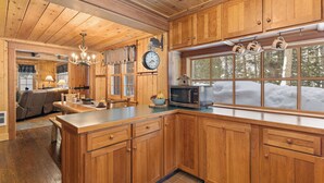 A wooden cabin interior with a kitchen featuring a large island, wooden cabinets, and a window overlooking a snowy landscape. - Double Loop (Island Park)