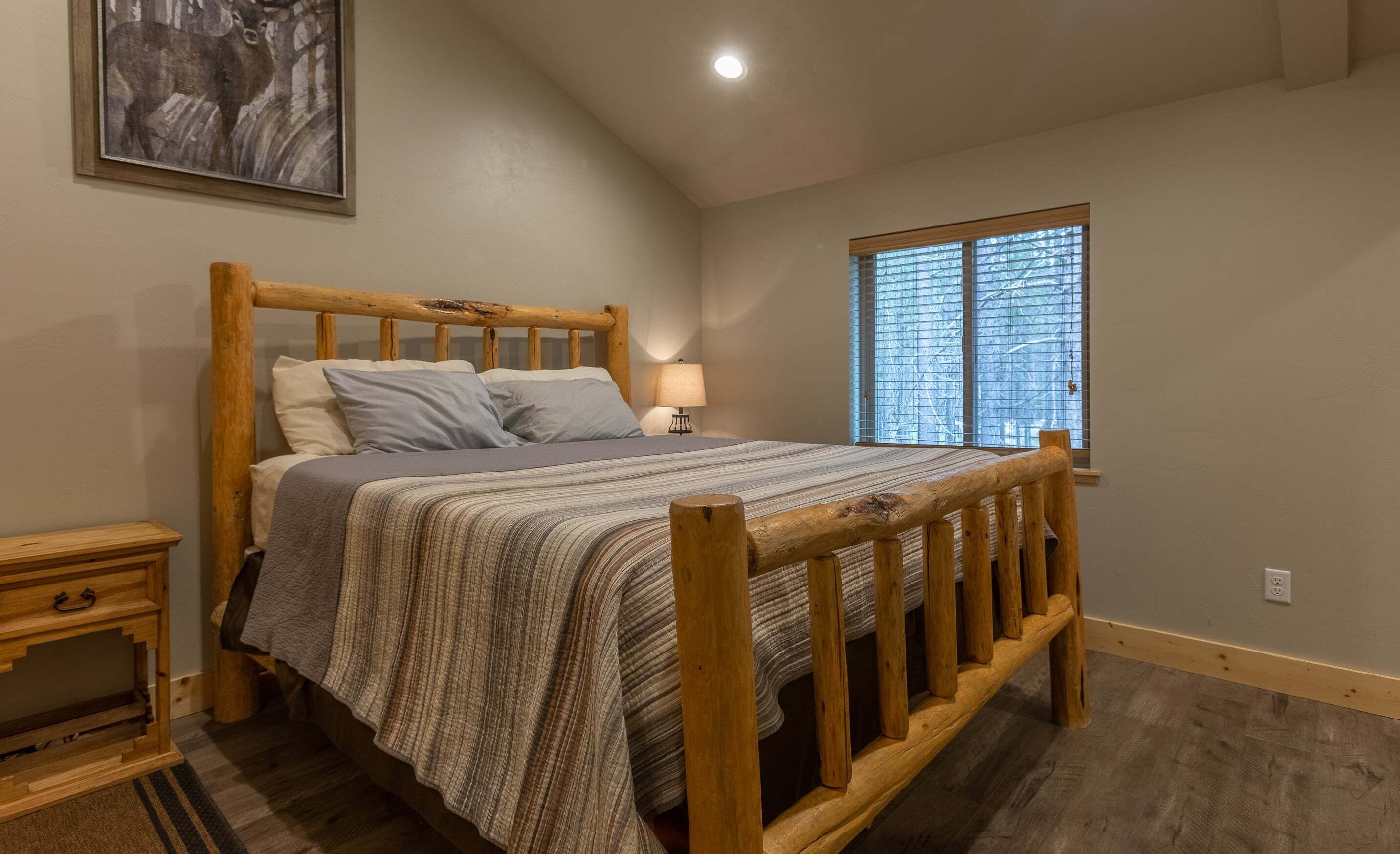 A wooden bed with a headboard, a bedside table, a lamp, and a window with blinds.