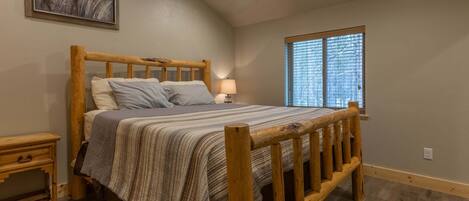 A wooden bed with a headboard, a bedside table, a lamp, and a window with blinds.