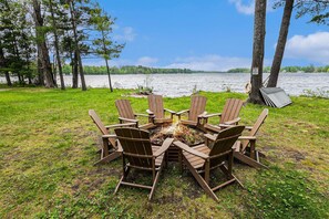 A circular wooden table with chairs around it, set on a grassy area near a lake with trees in the background. - Relax & Explore Waterfront Crawford Lake Cottage 4878 (Kalkaska)