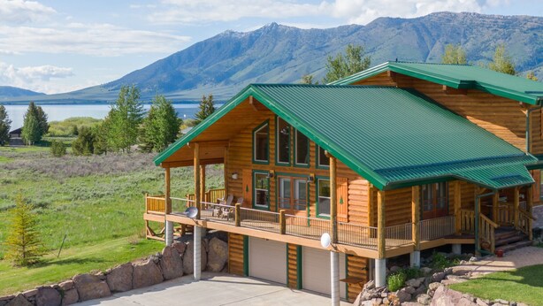 Une cabane en rondins avec un toit végétalisé, un balcon agrémenté de mobilier d’extérieur et une vue sur les montagnes et un lac.
