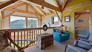 A cozy room with a wooden ceiling, a large window overlooking a lake, a blue sofa, and a rustic chest of drawers. - Henrys Lake Goose Bay (Island Park)