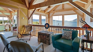 A cozy room with wooden beams, a view of the water, a green sofa, and a wooden chest. - Henrys Lake Goose Bay (Island Park)