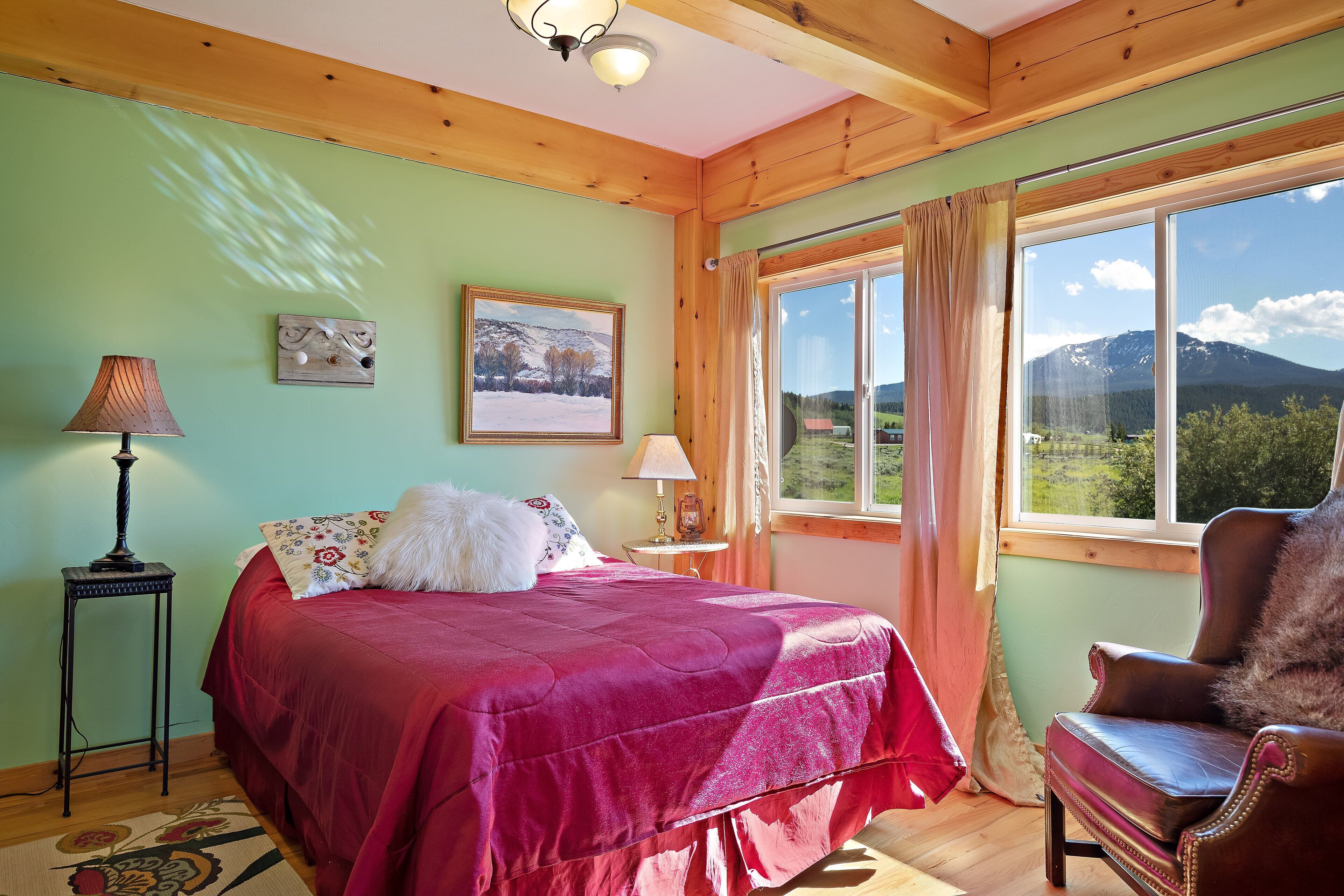 A bedroom with a bed, a chair, a lamp, and a window with a mountain view.