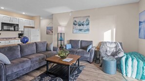 A modern living room with grey sofas, a wooden coffee table, and a blue ottoman. - Torch Lake Vista A Ga Ming Golf Retreat 741 Unit 9B (Kewadin)