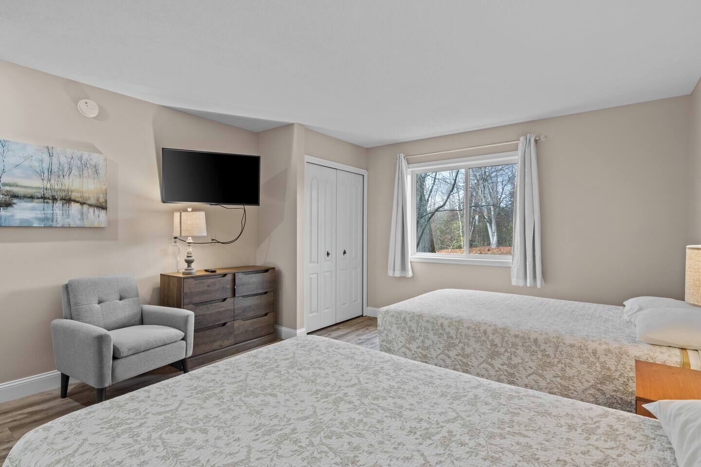 A bedroom with two beds, a chair, a dresser, a TV, and a window with curtains.