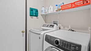 A laundry area with two washing machines, a shelf with laundry supplies, and a green electrical box. - Torch Lake Vista A Ga Ming Golf Retreat 741 Unit 9B (Kewadin)