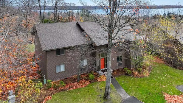 A two-story house with a red door, surrounded by a well-maintained lawn and autumn foliage. - Torch Lake Vista A Ga Ming Golf Retreat 741 Unit 9B (Kewadin)