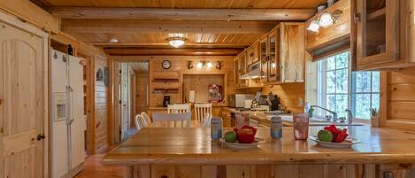 A wooden cabin interior with a kitchen area featuring a wooden countertop, a sink, and a dining table with chairs.