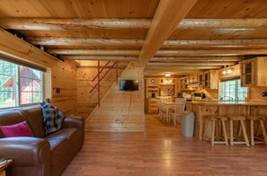 A wooden cabin interior with a living room, kitchen, and a staircase leading to the upper floor. - Hooter Hollow (Island Park)