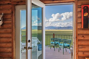 Eine Holzhütte mit Glastür, die auf eine Terrasse mit Korbmöbeln und Bergblick führt.