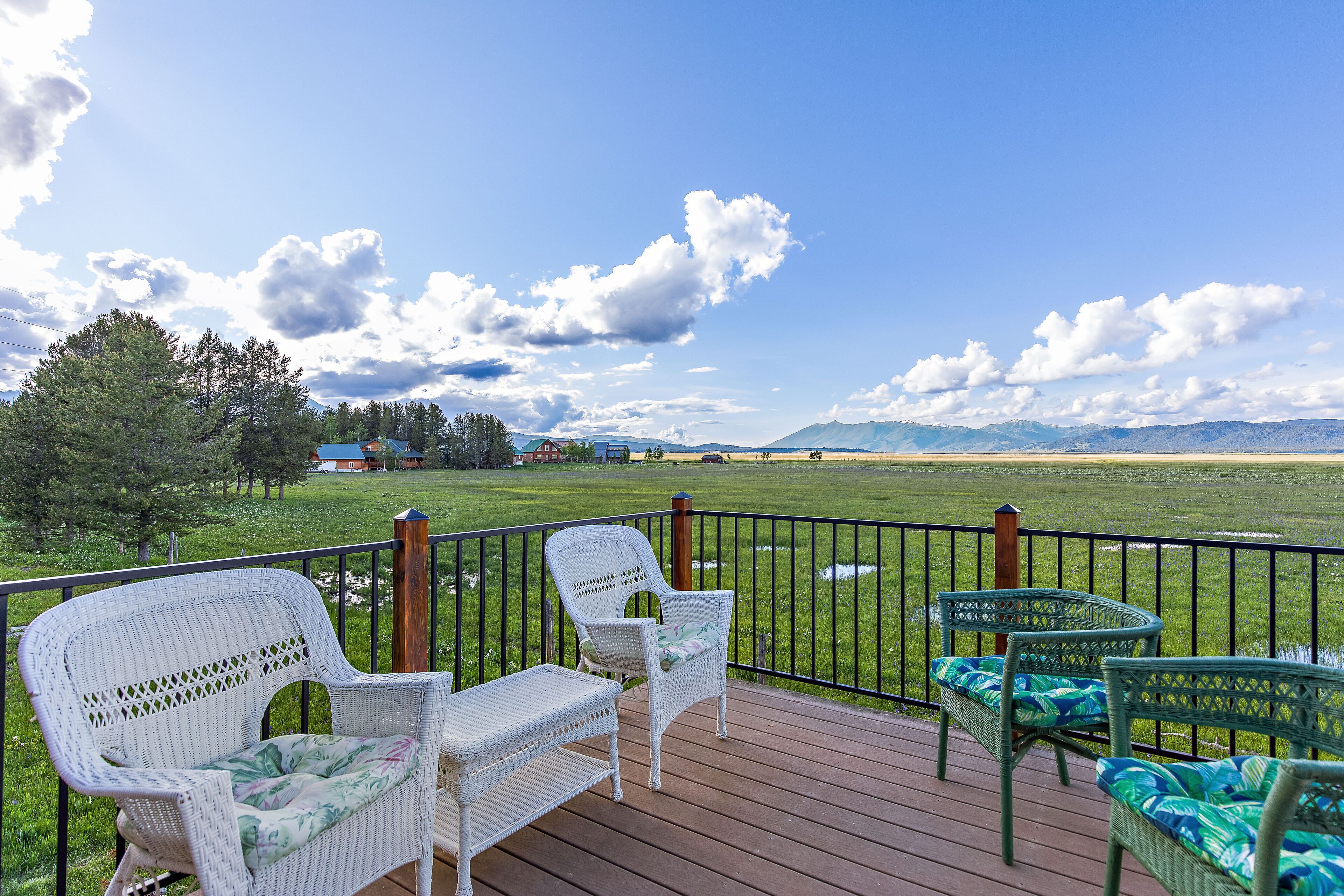 A deck with wicker furniture overlooking a grassy field and distant mountains.