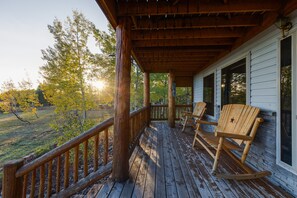 Eine hölzerne Veranda mit Schaukelstühlen, einem Holzaumschlag und Blick auf einen bewaldeten Bereich.