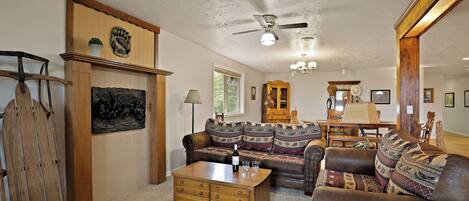 A cozy living room with a wooden coffee table, leather sofas, a wooden cabinet, and a ceiling fan.