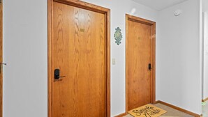 Un pasillo con dos puertas de madera, un cartel de bienvenida y un felpudo.