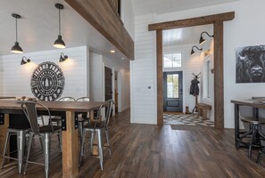Un comedor amplio con una mesa de madera y sillas metálicas, un reloj de pared grande e iluminación colgante.