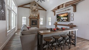 A spacious living area with a fireplace, a large window, and a wooden ceiling. - Cast Iron Moose (Island Park)